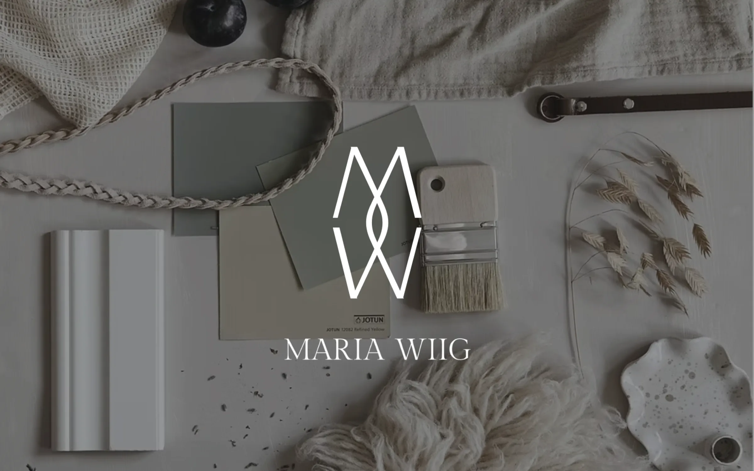 Maria Wiigs logotyp och symbol i vitt över en komposition med färgprover, pensel och torkade växter.